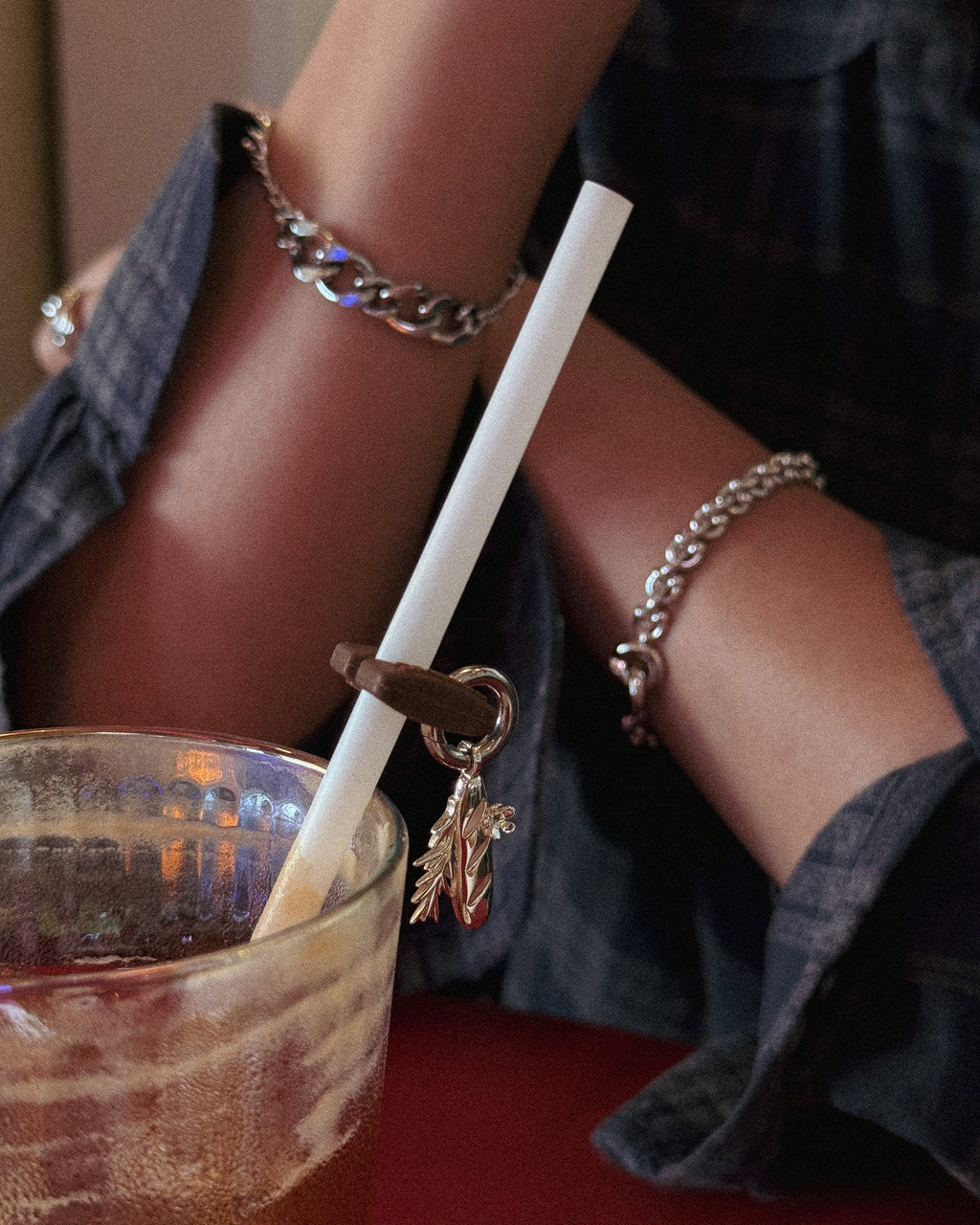 Ankle and wrist wearing Kiki's charms beside a drink in a warm interior
