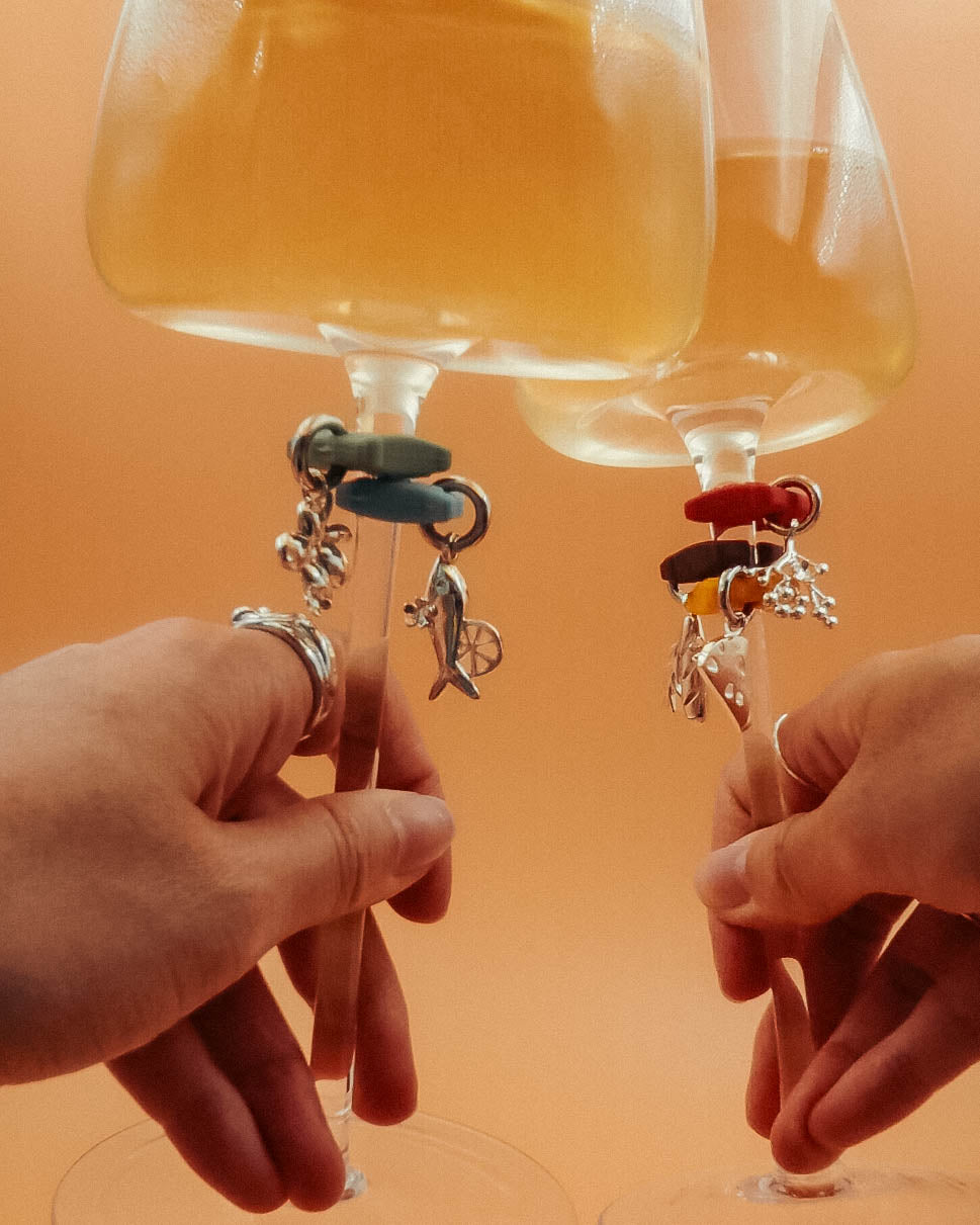 Two hands clinking wine glasses fitted with Kiki's hanging charms